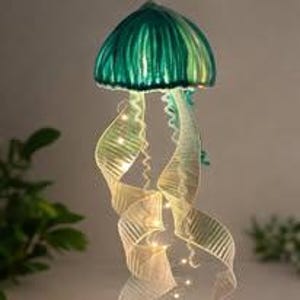 May include: A decorative jellyfish sculpture with a teal-green cap and flowing, ribbon-like tentacles. The tentacles are illuminated with small, warm white lights. The sculpture is designed to hang and adds a whimsical touch to any space.