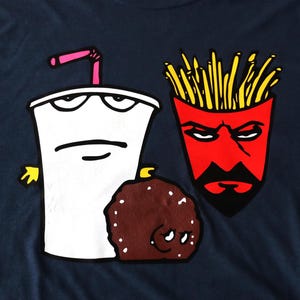 May include: Navy blue t-shirt featuring cartoon characters: a white milkshake with a pink straw, a red french fry container, and a brown meatball. The graphic design is in a bold, cartoon style.