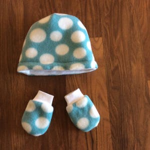 May include: A blue and white polka dot hat and matching mittens. The hat is folded down and the mittens are laying flat.
