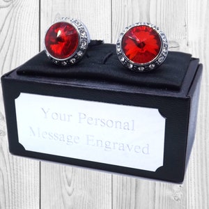 Peut inclure: Une paire de boutons de manchette avec des pierres de cristal rouges serties dans un métal argenté. Les boutons de manchette sont dans un coffret noir avec une plaque argentée qui indique "Votre message personnel gravé".