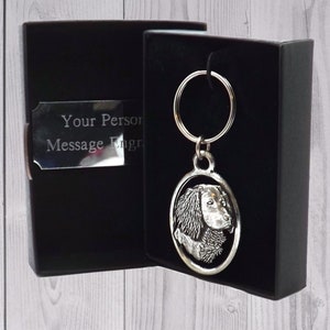 May include: A silver keychain with a round charm featuring a detailed profile of a dog's head. The keychain is in a black gift box with a silver plaque that says "Your Person Message Engraved".