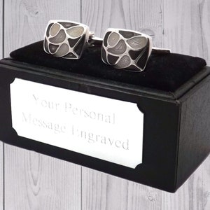 Puede incluir: Un par de gemelos negros y blancos en una caja de regalo negra con una placa plateada que dice "Su mensaje personal grabado".