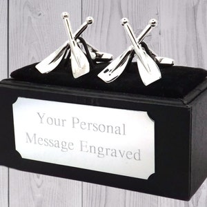 May include: Silver cufflinks in the shape of crossed oars, displayed in a black gift box with a silver plaque that reads "Your Personal Message Engraved".