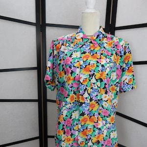 May include: A short-sleeved button-up shirt with a floral print in shades of pink, orange, yellow, blue, green, and white on a black background.