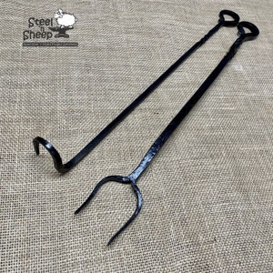 May include: A set of two black metal fireplace tools. The tools are hand-forged and have a rustic look. The tools are a poker and a log grabber. The tools are on a burlap background. Steel & Sheep Hand-Forged Goodness.