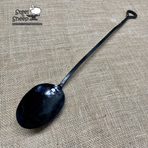 May include: A black metal fireplace shovel with a long handle and a rounded scoop. The handle has a twisted design and ends in a heart-shaped loop.