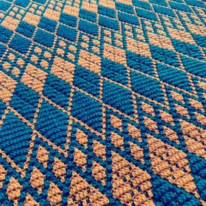 Puede incluir: Primer plano de una manta de ganchillo con un patrón de diamantes en tonos azul verdoso y marrón.