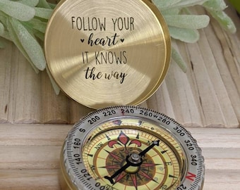 May include: A gold compass with a round, white face and black needle. The compass has a lid with the inscription "FOLLOW YOUR heart IT KNOWS the way".