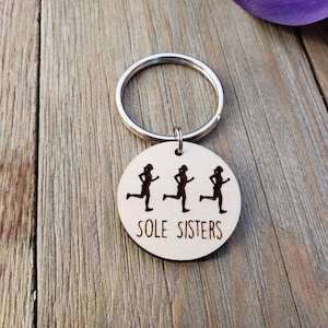 May include: A wooden keychain with three running figures and the text "SOLE SISTERS".
