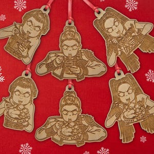 Peut inclure: Ornements de Noël en bois avec une illustration de dessin animé d'une personne mangeant des nouilles, avec le texte "Merry Xmas" sur certains. Les ornements sont sur un fond rouge avec des flocons de neige blancs et le mot "HUNTRAX" en vert.