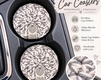 May include: Two round, crocheted car coasters in a variegated grey and cream yarn pattern, each featuring a small metal tag embossed with a heart icon and the text Made with LOVE, placed inside a black plastic vehicle cup holder console.
