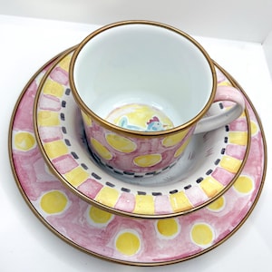 May include: A three-piece ceramic tea set with a pink, yellow, and white polka dot design. The set includes a teacup, a saucer, and a small plate. The teacup and plates have gold rims. The teacup has a small rooster illustration inside.