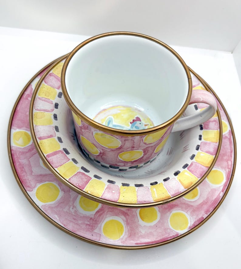 May include: A three-piece ceramic tea set with a pink, yellow, and white polka dot design. The set includes a teacup, a saucer, and a small plate. The teacup and plates have gold rims. The teacup has a small rooster illustration inside.