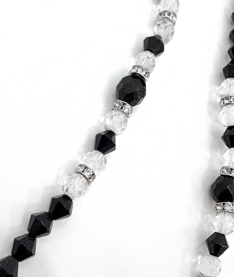 May include: A necklace with alternating black and clear faceted beads. The clear beads are separated by silver-toned spacers. The necklace has a classic design, suitable for various occasions.