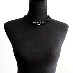 May include: A black beaded necklace with silver accents, displayed on a black mannequin. The necklace features two strands of small, dark beads and several larger, decorative silver beads.