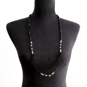 May include: A long black beaded necklace with silver accents, displayed on a black mannequin. The necklace features small, faceted black beads with sections of silver-coloured beads.