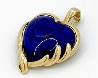 May include: A heart-shaped pendant featuring a deep blue stone, set within a gold-coloured frame. The pendant includes a loop for a chain and the text "Call Me For Treasure".
