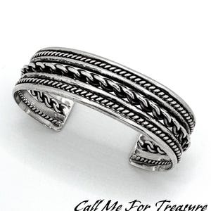 Puede incluir: Pulsera de brazalete de plata con un diseño trenzado. La pulsera tiene cuatro filas de metal trenzado.