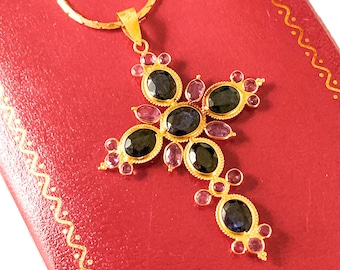 May include: A gold chain necklace with a pendant in the shape of a cross. The cross is adorned with dark blue and pink gemstones.