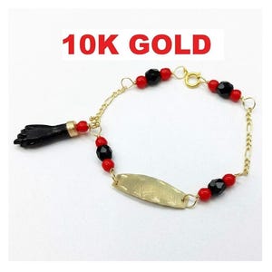 May include: A 10K gold bracelet featuring a black hand-shaped charm, a central gold plate, and alternating red and black beads. The chain is made of gold links and includes a spring ring clasp. The text 10K GOLD is visible above the jewelry.