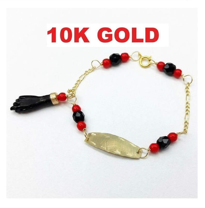 May include: A 10K gold bracelet featuring a black hand-shaped charm, a central gold plate, and alternating red and black beads. The chain is made of gold links and includes a spring ring clasp. The text 10K GOLD is visible above the jewelry.