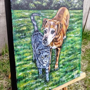 May include: A painting of a brown and white dog and a gray cat standing on green grass. The dog is looking at the viewer, while the cat is looking to the side. The painting is on a canvas and is framed in black.