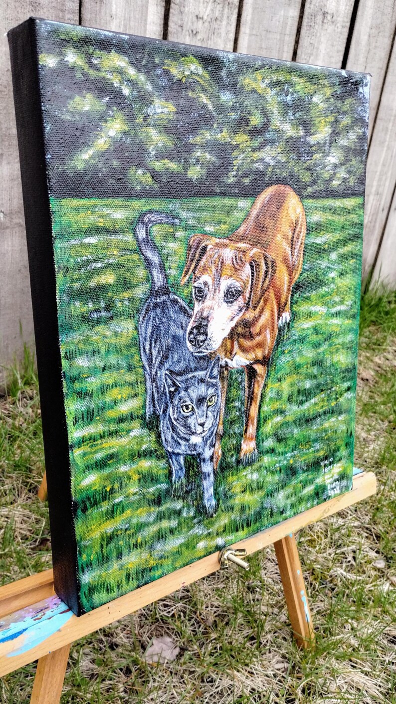 May include: A painting of a brown and white dog and a gray cat standing on green grass. The dog is looking at the viewer, while the cat is looking to the side. The painting is on a canvas and is framed in black.