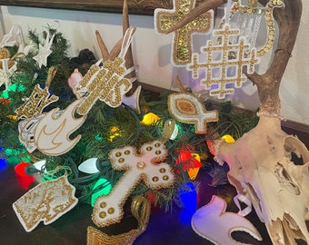 Könnte beinhalten: Eine Sammlung von weißen und goldenen Perlenornamenten, darunter Kreuze, Sterne und andere religiöse Symbole, die an einem Hirschgeweih hängen. Die Ornamente sind mit goldenen Perlen und Pailletten verziert.