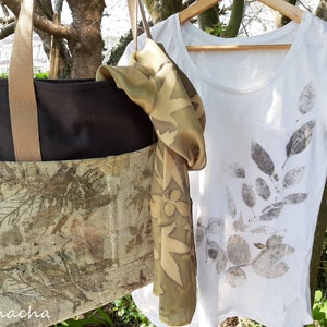 May include: A black tote bag with a brown strap and a green and brown floral print on the front. A white t-shirt with a green and brown leaf print is hanging on a wooden hanger. A green and brown floral print scarf is draped over the hanger.