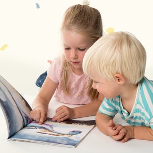 Peut inclure: Deux enfants, une fille aux cheveux blonds et un gar&ccedil;on aux cheveux blonds, sont assis sur le sol et regardent un livre ensemble. Le livre est illustr&eacute; de couleurs vives et est ouvert &agrave; une page avec une image d'une baleine.