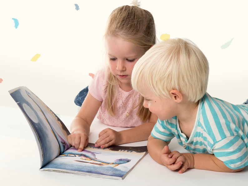 Peut inclure: Deux enfants, une fille aux cheveux blonds et un gar&ccedil;on aux cheveux blonds, sont assis sur le sol et regardent un livre ensemble. Le livre est illustr&eacute; de couleurs vives et est ouvert &agrave; une page avec une image d'une baleine.
