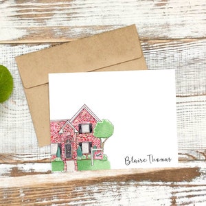 May include: A watercolor illustration of a red brick house with a green lawn and a "Sold" sign. The illustration is on a white card with the name "Blair Thomas" written in black ink.