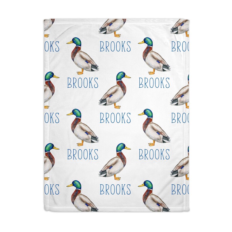 May include: White baby blanket with a repeating pattern of watercolor ducks and the name "Brooks" in blue text.