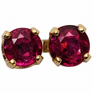 Puede incluir: Un par de pendientes de botón con piedras preciosas redondas de color rojo intenso engastadas en garras doradas. Los pendientes tienen un diseño clásico, con las piedras preciosas de aproximadamente 0,6 cm de diámetro.