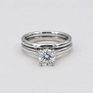 May include: A two-piece, silver-colored ring set. The engagement ring features a large, round, clear gemstone. The band is smooth and polished. The wedding band is a simple, matching band. The set is displayed on a white background.