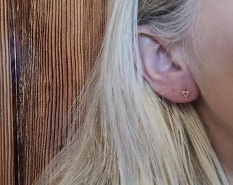 Könnte beinhalten: Nahaufnahme eines Ohrs mit einem kleinen goldenen Dreiecks-Ohrring.