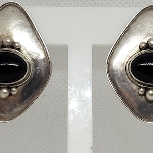 May include: A pair of silver earrings with black gemstone accents. The earrings are shaped like diamonds and have a silver bezel setting around the black gemstones.