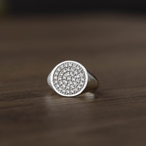 May include: A silver ring with a round face set with small, clear stones.