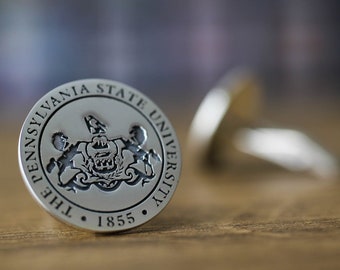 May include: A silver-colored circular pin with the text "The Pennsylvania State University" and the year "1855" around a crest.