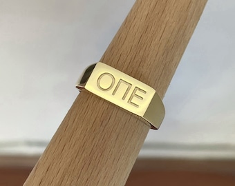 May include: A gold band ring with the word "ONE" engraved on the top.