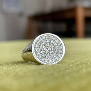 May include: A silver signet ring with a round face set with small, clear diamonds.