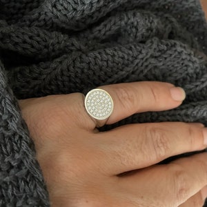 May include: A silver ring with a round, pave-set diamond top.