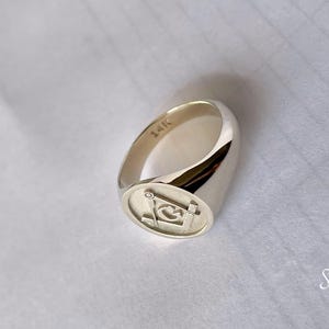 May include: A silver signet ring with a square Masonic symbol engraved on the face. The ring is marked "14K" on the inside band.