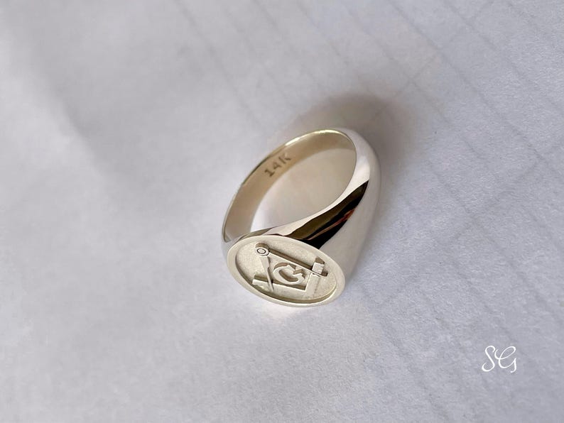 May include: A silver signet ring with a square Masonic symbol engraved on the face. The ring is marked "14K" on the inside band.