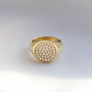 May include: A gold signet ring with a round, pave-set diamond top.