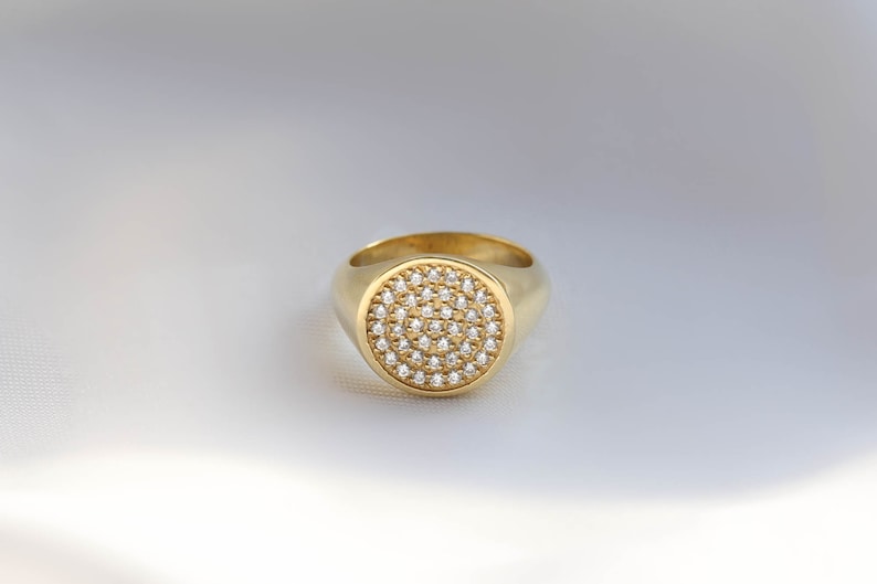 May include: A gold signet ring with a round, pave-set diamond top.