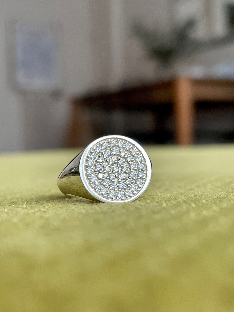 May include: A silver signet ring with a round face set with small, clear diamonds.