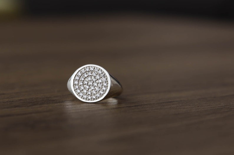May include: A silver ring with a round face set with small, clear stones.