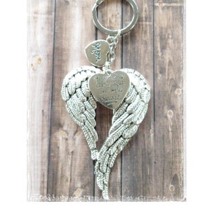 May include: Silver angel wing keychain with a heart charm that says "You are always in my heart". The keychain is on a wooden background.