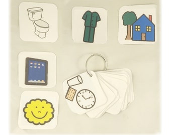 May include: A set of picture cards with various images, including a toilet, a shirt, a house, a tablet, a clock, a glass, a cracker, and a smiley face. The cards are attached to a ring.